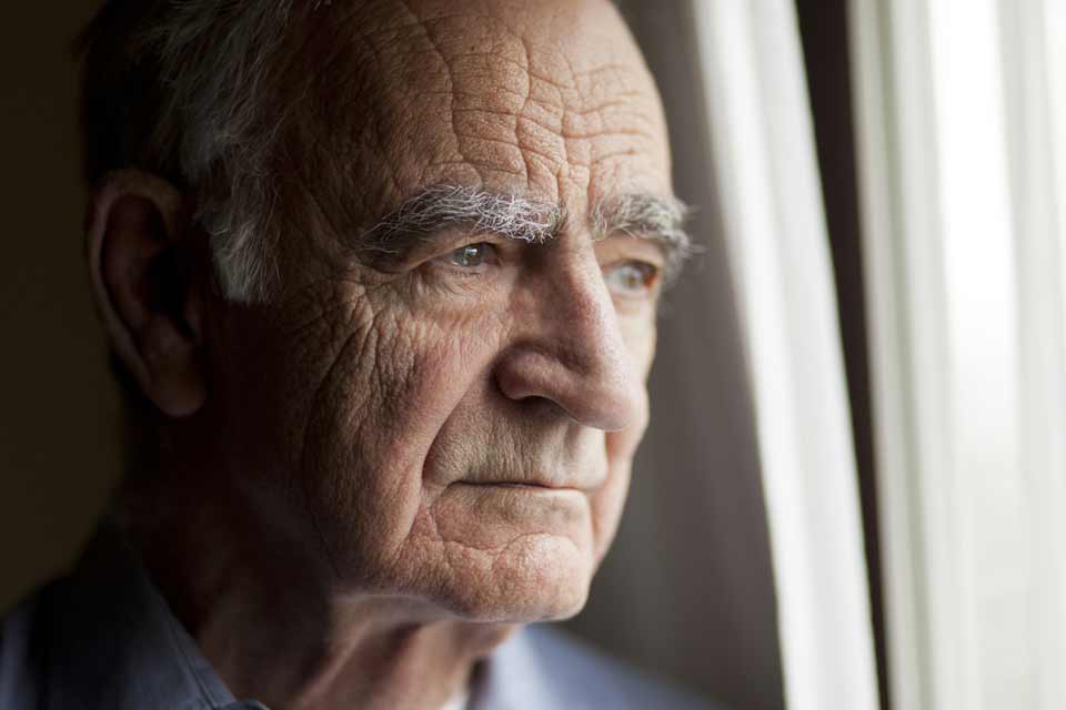 Elderly man looking forlornly out a window.